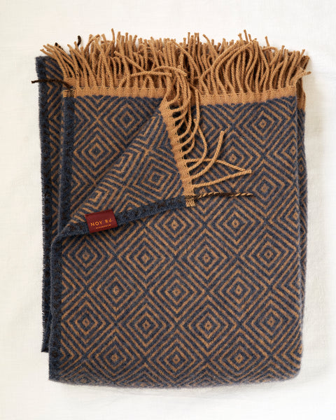 Folded blue blanket with geometric pattern and fringed edge on a white background