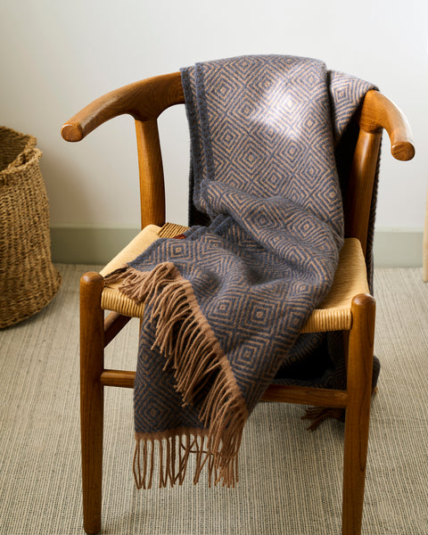Patterned blanket draped over a wooden chair with a woven basket in the background.