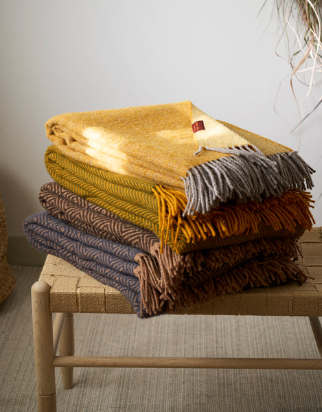 Stack of colorful woven blankets on a wooden chair against a neutral background