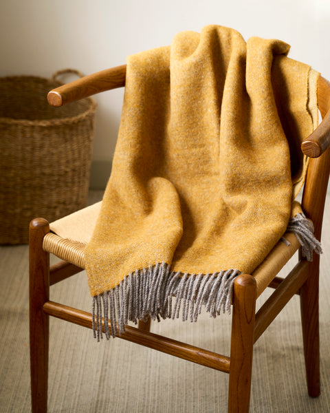 Yellow blanket with fringes draped over a wooden chair in a room.