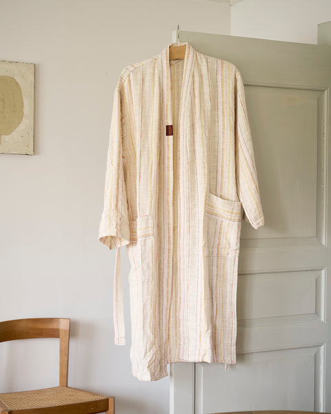 Beige striped robe hanging on a hook against a white wall.