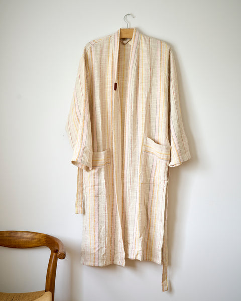 Beige striped robe hanging on a white wall with a wooden chair in the foreground.