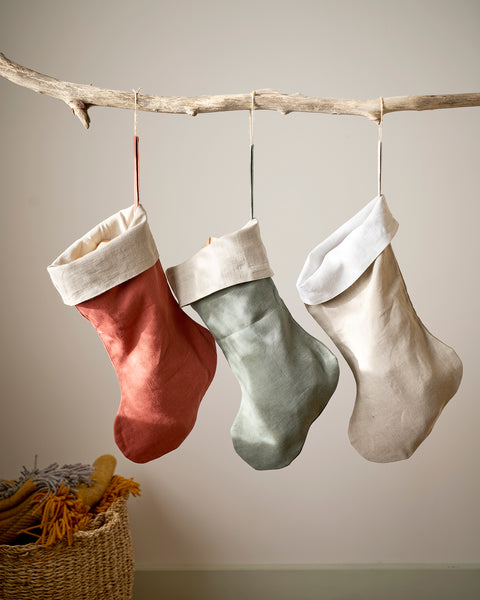 Three colorful stockings hanging on a branch against a plain wall.
