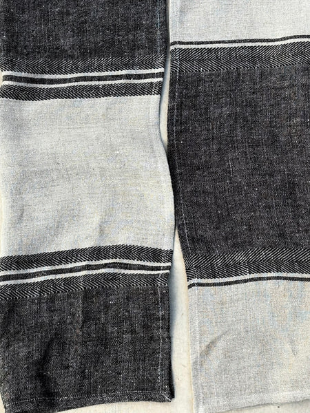 A close-up of a woven textile, likely a towel , featuring alternating wide panels of light gray and dark charcoal gray with thin white stripe accents.
